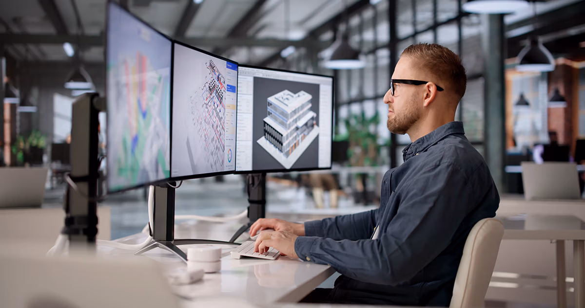 Engineer reviewing 3D building models across three monitors